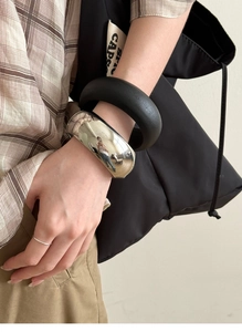 Polished metal cuff and black matte bangle set styled with a plaid shirt and ring