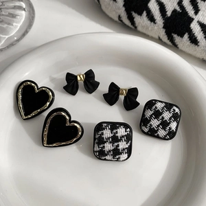 Retro houndstooth and heart stud earrings set in gold and black finish on a white plate