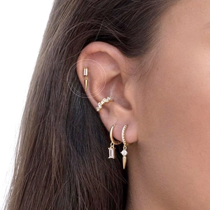 Close-up of gold geometric earrings with clear zircon stones and conical charms on ear