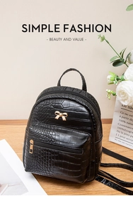 Detail view of mini black backpack featuring faux crocodile texture and gold bow ornament