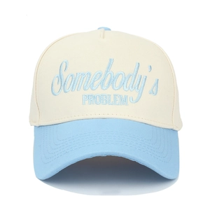 Close-up of Somebody's Problem embroidery on a cream and light blue trucker hat