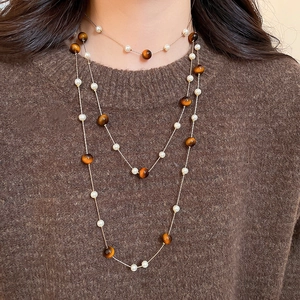 Detail einer mehrlagigen Goldkette mit weißen Perlen und Tigerauge auf braunem Pullover