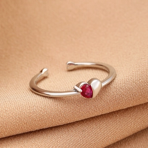 Macro shot of silver adjustable ring featuring a heart-shaped red zircon on silk fabric
