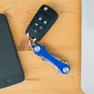 Blue metal key organizer with silver keys on a wooden desk with a phone and laptop