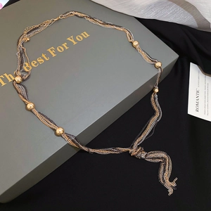 Detail of multi-layer metallic chain necklace with knotted tassel on a gray gift box
