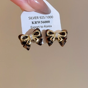 Detail of bow-shaped stud earrings in tortoiseshell resin with gold trim and zircon