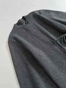 Detail of dark grey knit coat featuring ribbed round neck and amber button closure
