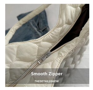 Detail of smooth silver metal zipper and quilted texture on a white nylon tote bag
