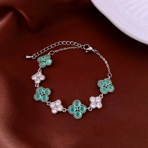 Detail of four-leaf clover bracelet with green gems and zircon stones on silk background