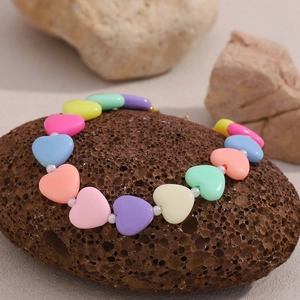 Detailed macro shot of a colorful heart-shaped beaded bracelet on a dark textured rock