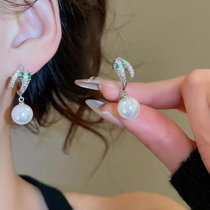 Detail of 14K gold plated earrings featuring green gemstone eyes and large white pearls