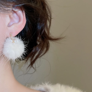 Macro shot of a white faux fur pompom earring with delicate rhinestone stud on person