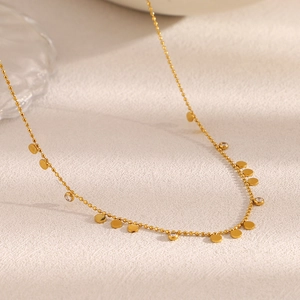 Détail du collier en acier plaqué or 18K avec perles et disques en zircon sur tissu