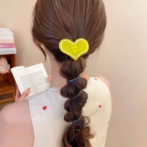 Détail d'un élastique à cheveux cœur en acrylique jaune avec surpiqûres sur une tresse
