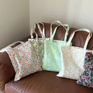 Close-up of assorted floral and textured cotton tote bags on a leather sofa surface