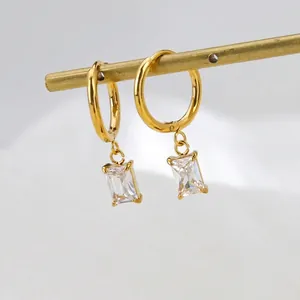 Gold hoop earrings with square zircon pendant hanging on a metal rod against grey background
