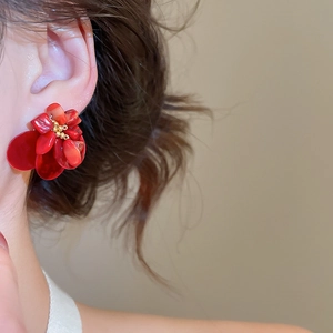 Close-up of a model wearing a textured red floral earring with gold bead details