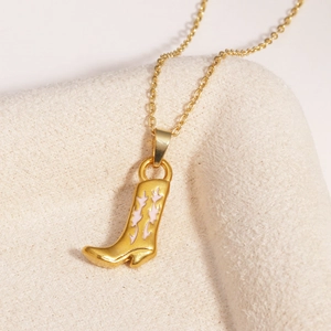 Détail d'un pendentif botte de cow-boy doré avec émail rose sur un tissu beige doux