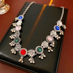 Macro detail of vintage floral necklace with colorful gems and tiny metal bell pendants