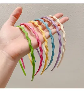 Detailed view of seven candy-colored wavy headbands held in hand showing glossy finish