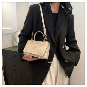 Detail of cream crossbody bag with 'M' pattern on a model wearing a black blazer
