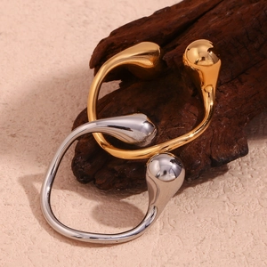 Detailed close-up of gold and silver water drop open rings on a natural wood piece