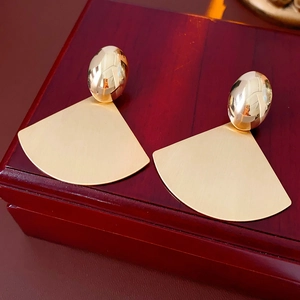 Detail showing the matte brushed metal texture of golden fan-shaped drop earrings
