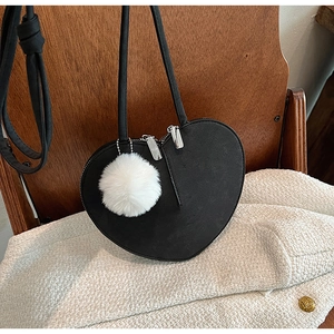 Detail einer matten schwarzen Herz-Umhängetasche mit weißem flauschigen Bommel-Anhänger