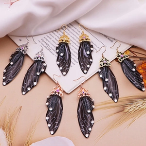 Detail of colorful cicada wing earrings with white rhinestones on vintage book pages