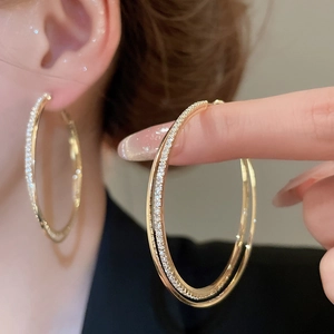Close-up of golden double-layered interlaced hoop earrings with inlaid rhinestones