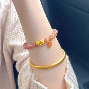 Close-up of pink sunstone beaded bracelet with golden Pixiu charm and matte gold bangle