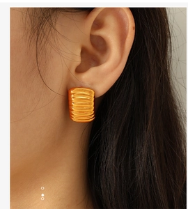 Close-up of golden chunky rectangular hoop earrings with horizontal ribbed texture on ear