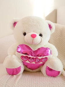 Detail of white teddy bear with pink metallic ears holding a heart-shaped LOVE pillow