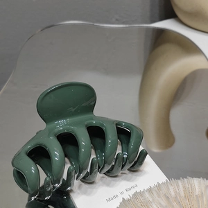 Detailed close-up of a glossy dark green shark hair claw clip on a stylish mirror surface