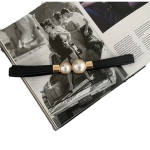 Elegant skinny black leather waist belt with gold double pearl buckle on a fashion magazine