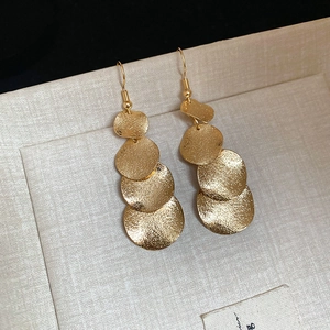 Close-up of golden sequin tassel earrings with hammered texture in a beige jewelry box