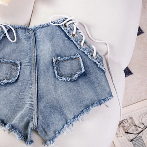 Dettaglio di pantaloncini di denim a vita alta con stringhe laterali e orlo grezzo sfilacciato