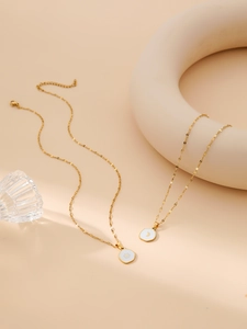 Close-up of gold stainless steel necklaces with sun and moon pendants on white enamel