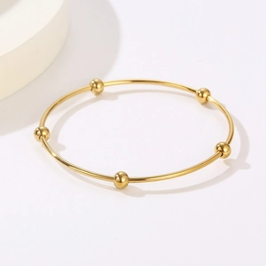 Detail of minimalist gold-plated stainless steel coil bracelet featuring five sliding beads