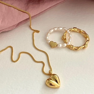 Close-up of golden heart pendant necklace and pearl ring on white and pink texture