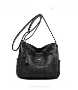 Close-up of black crossbody bag featuring functional zippers and plaid embossed texture