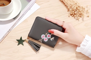 Detail of dark grey zip wallet with floral embroidery, leather tassel and star charm