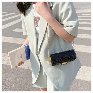 Detail of a quilted black patent leather cylinder bag with a gold chain and turn-lock