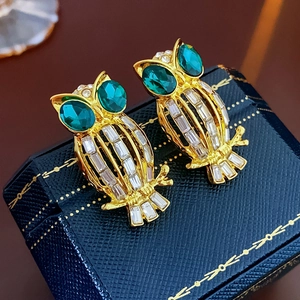Detailed macro view of vintage owl stud earrings with green gemstones on a blue jewelry box