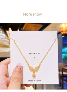 Macro detail of angel wing pendant with pink teardrop zircon and gold chain on card
