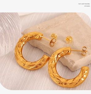 Detail showing gold C-shaped earrings with irregular hammered texture on a stone base