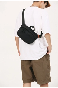 Close-up of black nylon crossbody bag with orange logo detail on back of a model