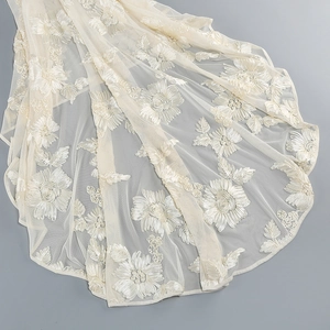 Detailed macro view of ivory lace embroidery with intricate floral patterns on mesh fabric