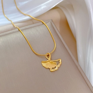 Macro shot of gold ginkgo leaf pendant necklace resting on a beige jewelry box