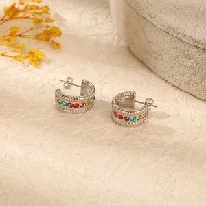 Macro detail of silver C-shaped stainless steel earrings with colorful crystals and braided edges